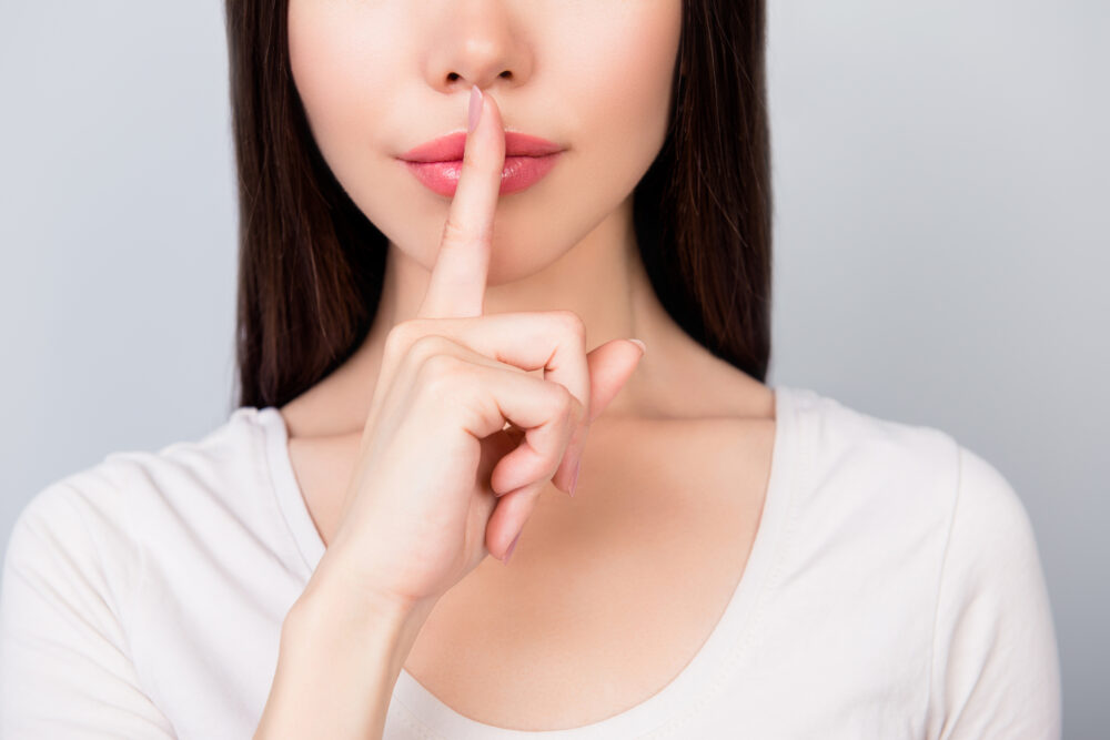 Shhh! Close up portrait of half face of young woman with  finger showing hush silence sign, gesture and beauty concept, grey background, nice girl asking for silence