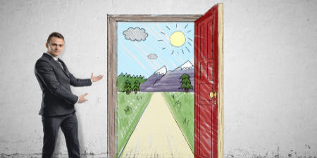 Businessman stands showing sunny scene with the road and mountains behind an open door by both hands