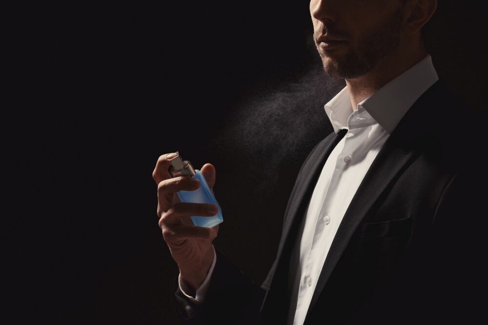 Handsome man using perfume on black background